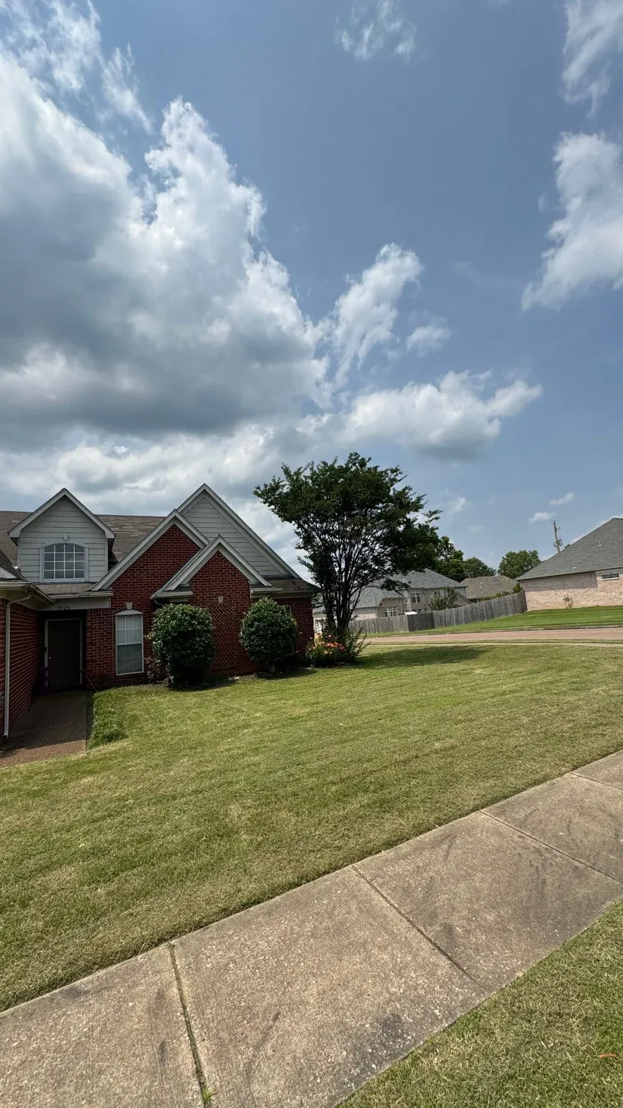 A brick residential home with a lush, manicured lawn and clean landscaping under a bright sky.