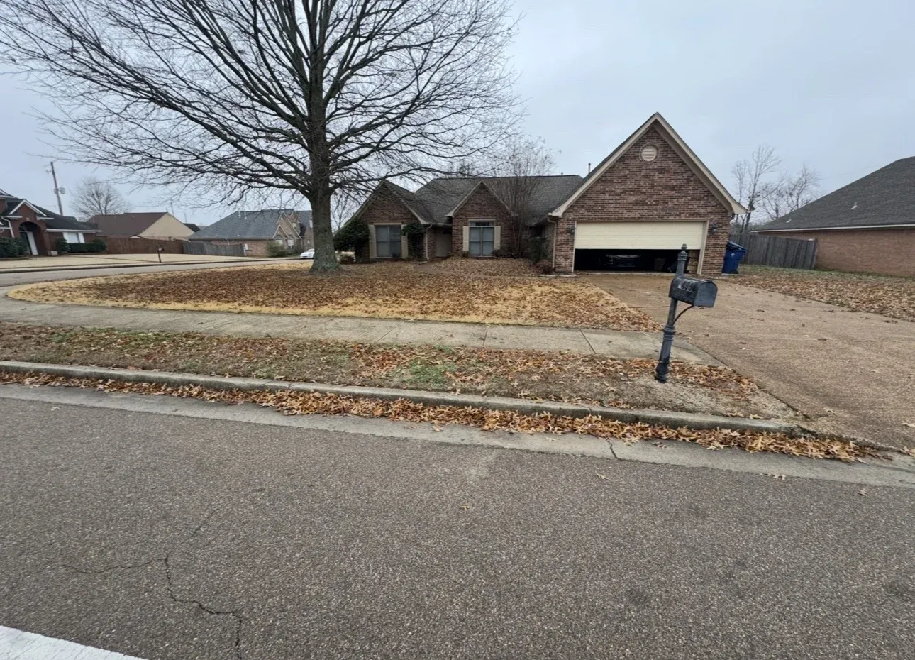 A suburban brick home with a tidy driveway and neatly maintained landscape in early spring.